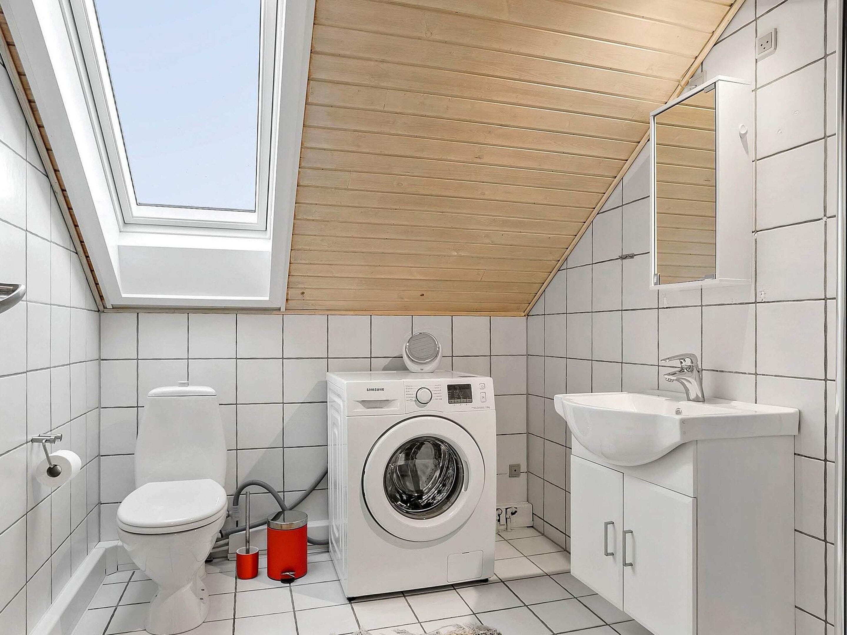 A compact bathroom with a skylight, a washing machine, a toilet, and a sink.