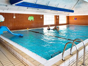 An indoor swimming pool with a blue slide, a lifeguard stand, and a brick wall with animal decorations.