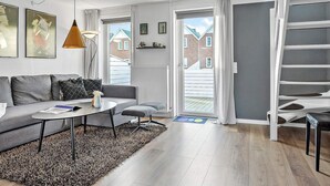 A modern living room with a sofa, coffee table, and a lamp. There is a staircase to the right and a door leading outside.