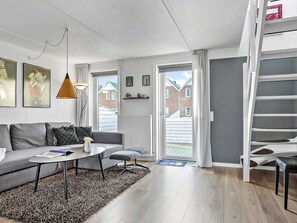 A modern living room with a sofa, coffee table, and a lamp. There is a staircase to the right and a door leading outside.