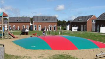 A playground with a colorful play area, including a slide and swings, in front of residential buildings.