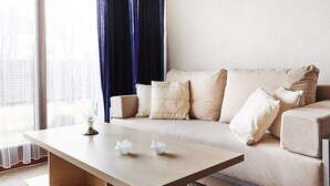 Ein modernes Wohnzimmer mit einem beige gefärbten Sofa, einem Holztisch und einem großen Fenster mit dunklen Vorhängen.