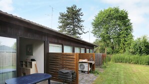 Ein kleines Haus mit einer Terrasse, einem Holzzaun und einem Garten.