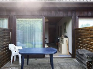 Un petit espace extérieur avec une table et des chaises, une porte-fenêtre coulissante donnant sur une cuisine et une clôture en bois.