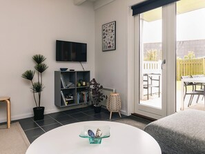 A modern living room with a flat-screen TV, a bookshelf, and a dining area visible through a sliding glass door. - 6 Person Holiday Home in Hadsund (Hadsund)