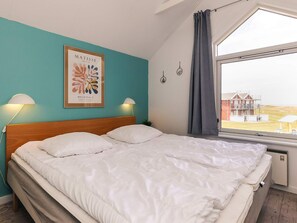 A bedroom with a wooden headboard, a large bed with white bedding, two bedside lamps, a framed artwork on the wall, and a window with a view of a building outside. - 6 Person Holiday Home in Hadsund (Hadsund)