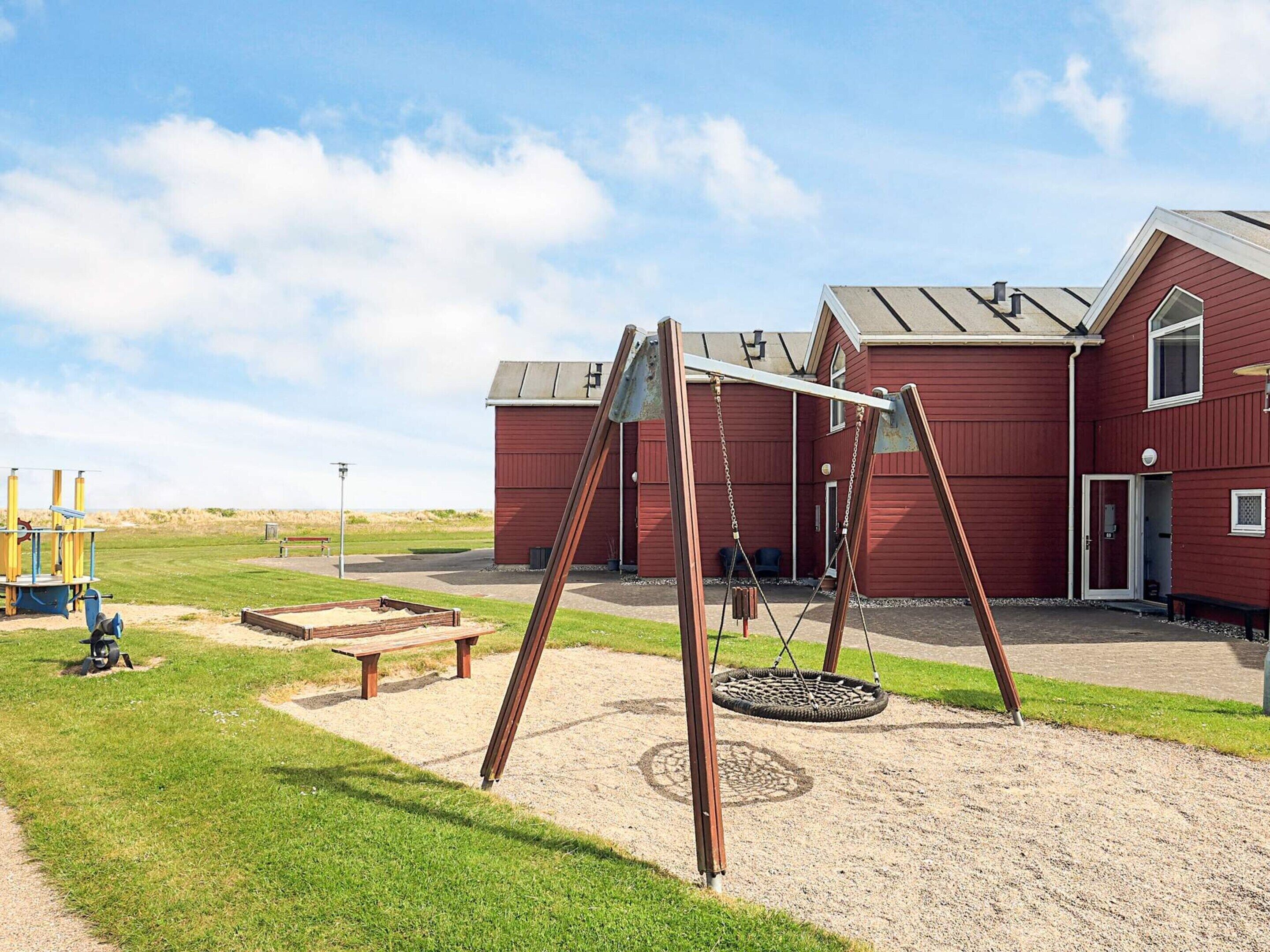 A playground with swings and a tire swing, a red building with a door, and a grassy area.