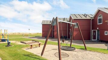 A playground with swings and a tire swing, a red building with a door, and a grassy area.