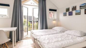 A bedroom with a bed, a desk, and a balcony with curtains.