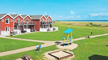 Um edifício vermelho com varanda, um parquinho com estrutura azul e vista clara para a praia.