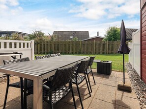 An outdoor patio with a wooden table and chairs, surrounded by a wooden fence and a grassy area.