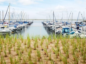 A marina with multiple boats docked, surrounded by sand and sparse grass. - 5 Star Holiday Home in Wendtorf (Wendtorf)
