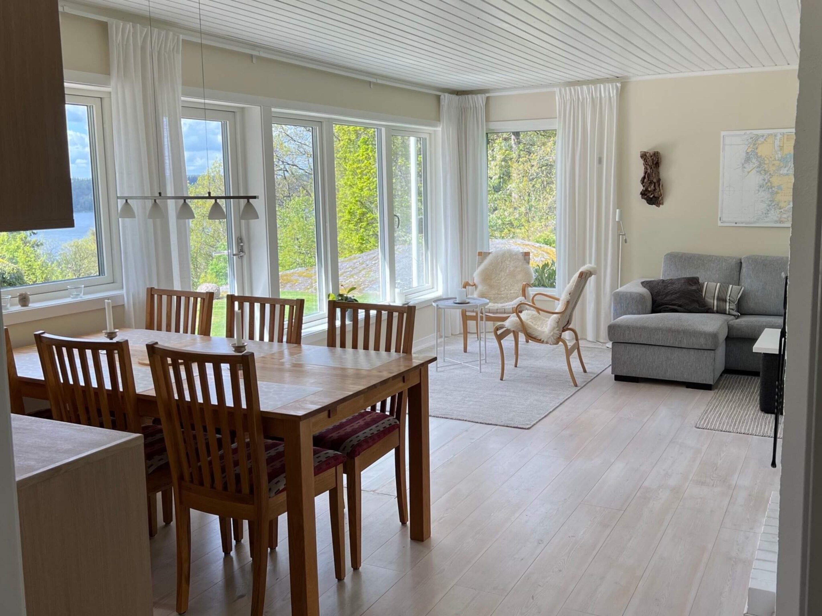 A modern living room with a dining area, large windows, and a view of the outdoors.