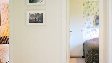 A room with a bed, a door leading to another room, and two framed pictures on the wall.