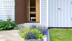 A wooden door leading to a porch with a bench, a fenced area with a gate, and a planter with blue flowers. - 4 Star Holiday Home in Ljungskile (Ljungskile)