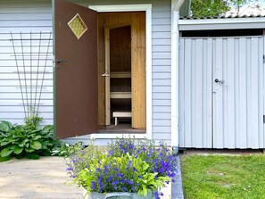 A wooden door leading to a porch with a bench, a fenced area with a gate, and a planter with blue flowers. - 4 Star Holiday Home in Ljungskile (Ljungskile)
