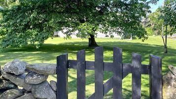 A stone wall with a wooden gate, a grassy area, and a large tree providing shade.