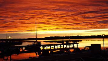 A sunset over a marina with boats docked, a pier extending into the water, and a distant shoreline.