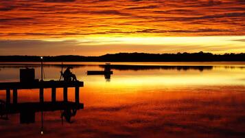 A sunset over a calm lake with a dock and a silhouette of a person.
