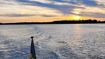 A body of water with a wake from a moving object, likely a boat, and a sunset in the background.