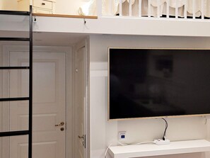 Quarto com televisão fixada na parede, uma porta branca e um console branco.