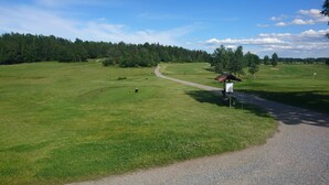 Golfkenttä, jossa on sorapolkua, pieni suojakatos ja lippu viheriöllä.