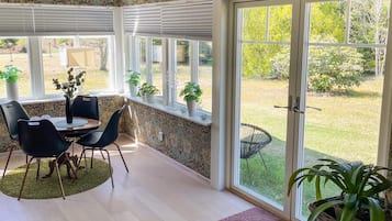 A room with a dining table, chairs, a potted plant, and a large sliding glass door leading to a garden.