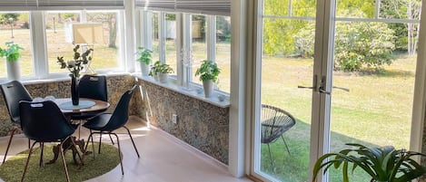 A room with a dining table, chairs, a potted plant, and a large sliding glass door leading to a garden.