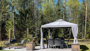 Ein Pavillon mit Tisch und Stühlen, umgeben von einer Holzterrasse und einem Grill.