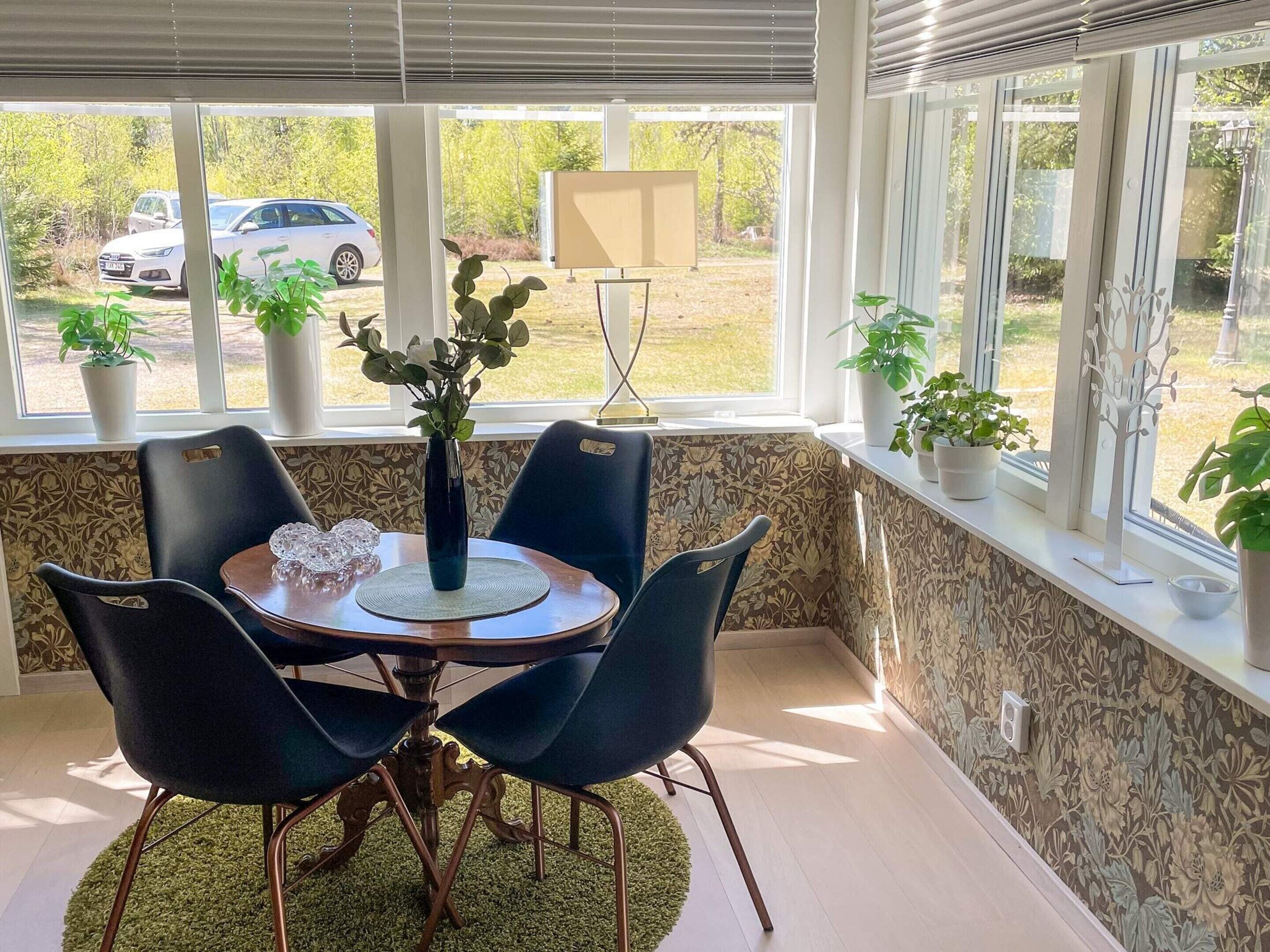 A dining area with a table, chairs, a vase with plants, and a view of parked cars outside.