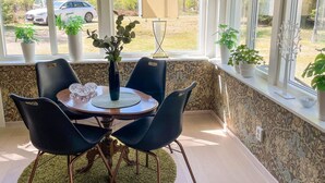Un coin repas comprenant une table, des chaises, un vase avec des plantes et une vue sur les voitures garées à l’extérieur.