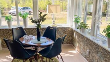 A dining area with a table, chairs, a vase with plants, and a view of parked cars outside.