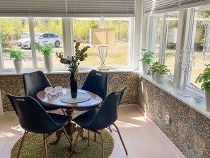 A dining area with a table, chairs, a vase with plants, and a view of parked cars outside.