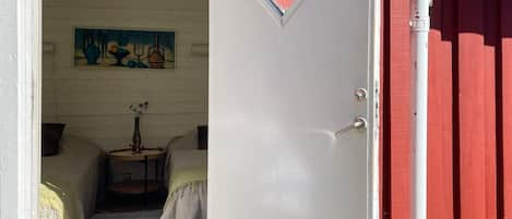 A room with a bed, a small table with a vase, and a painting on the wall.