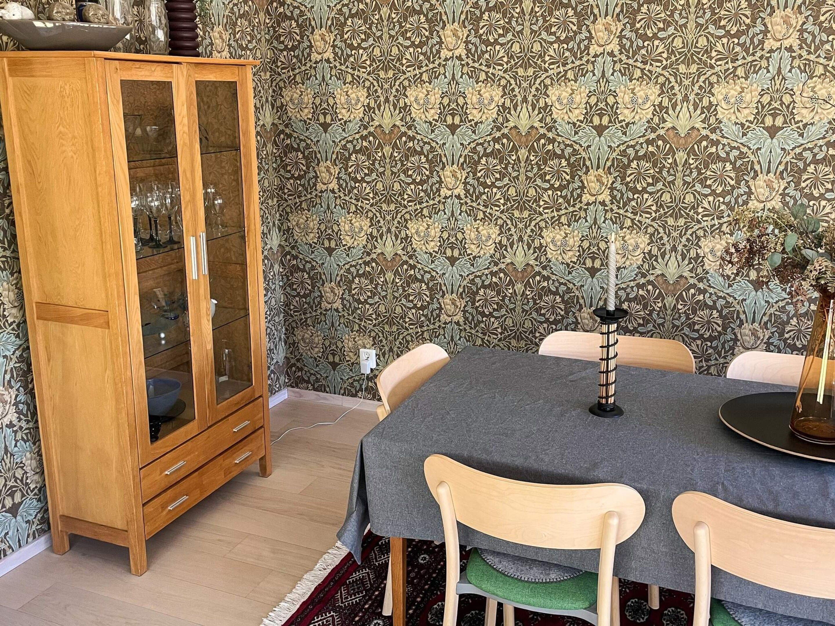 Un coin repas avec une table ronde, des chaises, un buffet en bois et un papier peint à motifs.