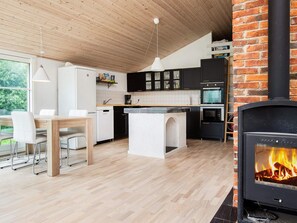 A modern kitchen with a central island, a dining area with chairs, and a fireplace.