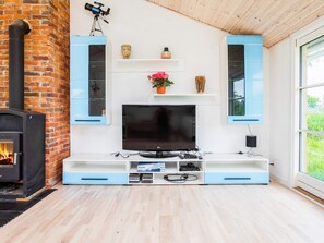 A living room with a TV, shelves, a fireplace, and a window. - 6 Person Holiday Home in Idestrup (Idestrup)
