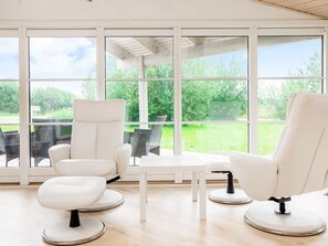 A modern room with large windows, two white armchairs, a small table, and a view of a green landscape.