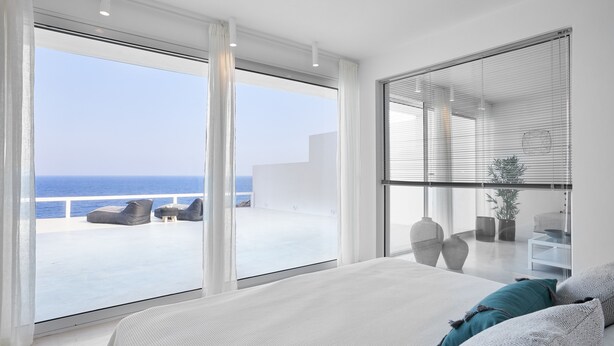 Quarto moderno com uma cama grande, vista para o mar e varanda com área de estar ao ar livre.