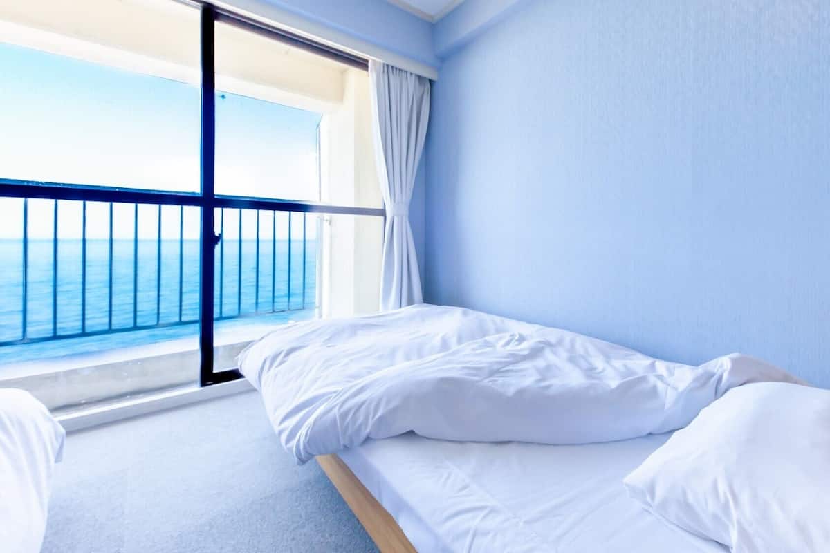 A single bed in a room with a view of the sea through a balcony.