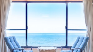 A room with two blue armchairs and a small wicker table, a large window with a view of the sea, and curtains on either side. - hotel onoura (Mihama)