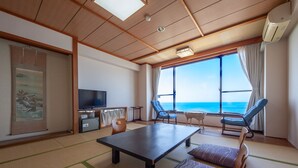 A room with tatami flooring, a television, a table, two chairs, and a view of the sea. - hotel onoura (Mihama)