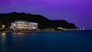 A coastal building with multiple floors, a stone wall, and a lighthouse in the background. - hotel onoura (Mihama)