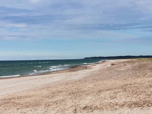 A wide sandy beach with gentle waves, a clear sky, and distant land.