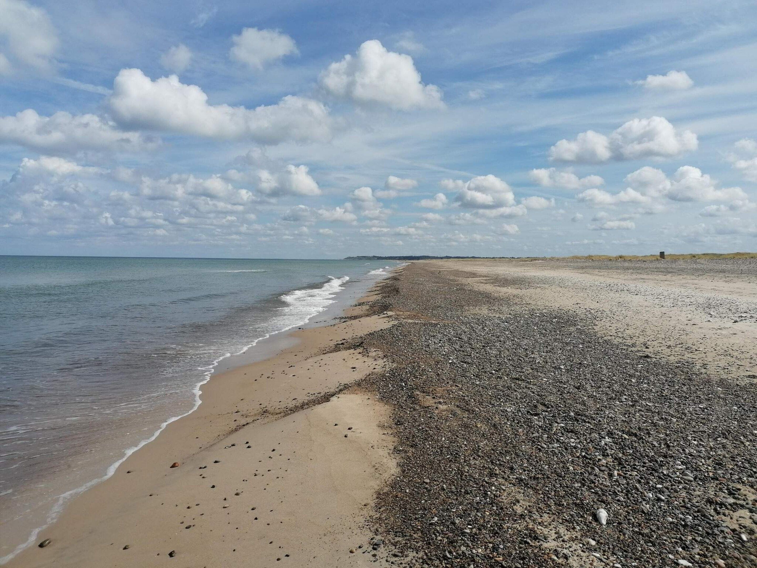 A beach with pebbles and sand, a clear sky, and distant land.