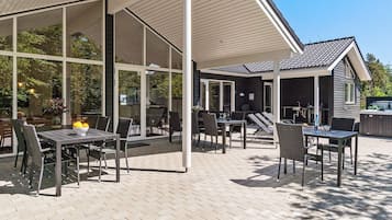 An outdoor patio area with tables and chairs, a covered seating area, and a hot tub.