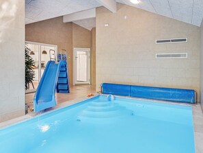 En inomhuspool med en blå vattenrutschkana, en stege och en bänk.