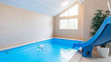 An indoor swimming pool with a slide, a potted plant, and a window.