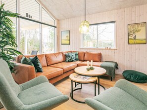 A cozy living room with a leather sofa, two armchairs, a round coffee table, and a hanging light fixture.