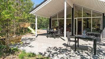 A covered outdoor patio with a table and chairs, a slide, and a wooden deck.